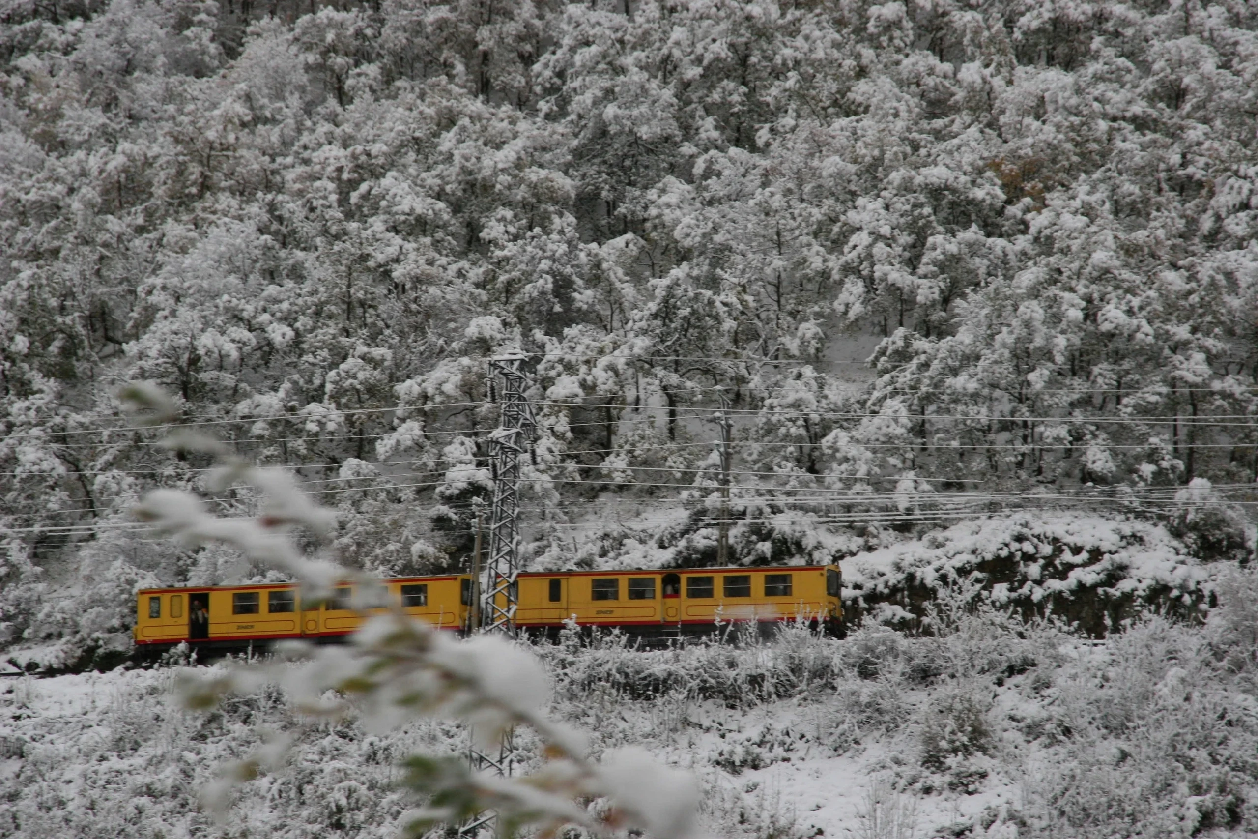 Train jaune traversant forêt enneigée en hiver